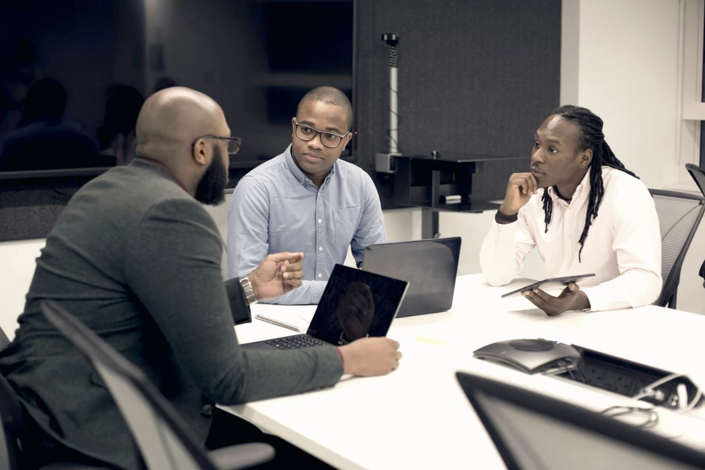 Three consultants in discussion around a meeting table with laptops