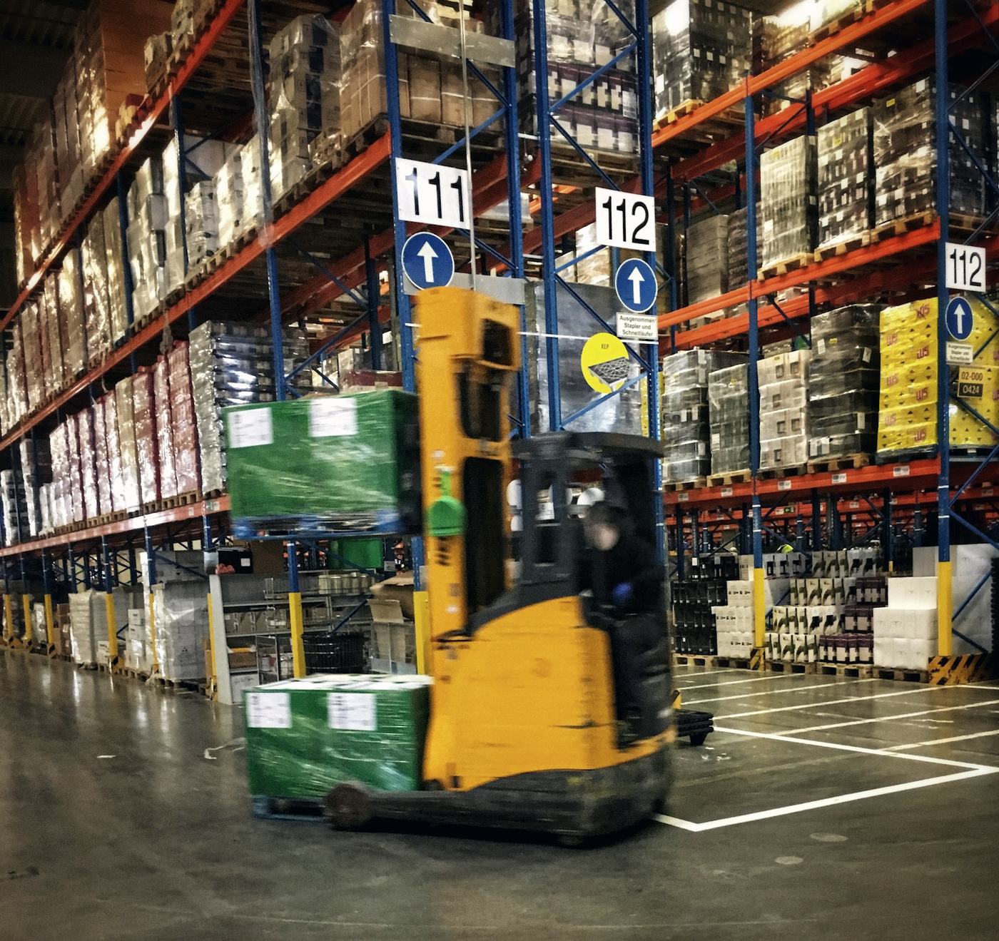 Forklift moving pallets between tall racks in a warehouse